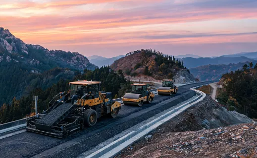 Asphalt paver convoy laying base course in mountain terrain
