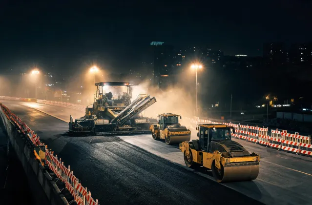 Night paving train with paver and tandem rollers under floodlights